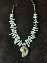 Collar corto con cuentas irregulares de nácar color blanco y dije de caracol con detalles dorados. Cierre con gancho y cadena de acero quirúrgico para regular el largo.