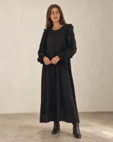 Vestido largo negro de algodón, con diseño amplio y fluido, mangas largas abullonadas con volados y textura sutil en la tela.