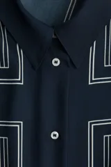 Camisa de sarga de corte oversized, color azul marino, con estampado geométrico de líneas blancas. Presenta cuello clásico, cierre frontal con botones, hombros caídos y mangas largas con puños abotonados.