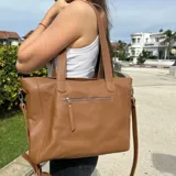 Cartera tipo tote de cuero natural color camel, con textura granulada. Cuenta con doble asa fija para llevar al hombro, correa larga ajustable y removible, cierre superior y bolsillo externo con cierre en la parte trasera.
