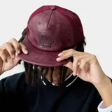 Gorra tipo trucker bordó, con frente de cuero sintético y paneles traseros de malla. Cuenta con visera plana y diseño con escudo bordado en la parte frontal.