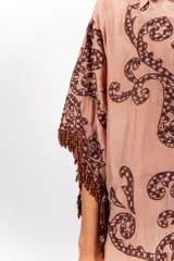 Vestido corto de silueta amplia, color tostado con bordados barrocos en contraste, escote en V con botones de madera, mangas anchas tipo capa con flecos de cuentas en los bordes.