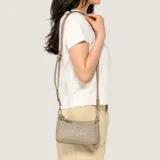 Cartera bandolera Guess modelo Holly, de diseño multicapa en color gris topo con grabado de monograma en relieve y herrajes plateados. Incluye correa ajustable con hebilla y el logo triangular distintivo de la marca en el frente.