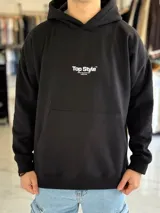 Canguro negro oversize con capucha y gran estampado blanco en la espalda con el texto "Top Style", "Dream big. Work hard. Make it real.", "SINCE 2021" y un código de barras.