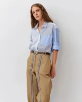 Camisa de corte recto y ligeramente oversize, confeccionada en algodón orgánico. Presenta un diseño a rayas con paneles en contraste de tonos azules y blancos, cuello clásico, cierre frontal de botones y un bolsillo en el pecho.