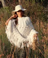 Poncho de lana merino color marfil, tejido a mano con diseño de puntos en relieve y largos flecos en los bordes.