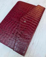 Funda para laptop de cuero con textura de reptil en color bordó, con cierre de solapa y botón metálico.