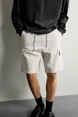 Bermuda cargo color negro de corte relaxed fit, confeccionada en tejido de algodón con elasticidad y efecto lavado. Cuenta con cintura elástica ajustable con cordón, bolsillos frontales y bolsillos laterales tipo cargo con solapa en las perneras.
