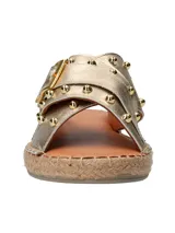 Sandalias tipo ojota con tiras cruzadas en cuero metalizado dorado, decoradas con tachas metálicas y hebilla lateral. Presentan una base con detalle de yute trenzado alrededor del contorno.