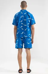 Short de algodón azul con estampado de sirenas blancas, corte relajado y largo hasta la rodilla. Tiene cintura elástica con cordón ajustable, dos bolsillos laterales y un bolsillo trasero tipo parche.