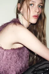 Top de cuello redondo y manga sisa, confeccionado con un acabado de flecos largos en color lila. Presenta un diseño recto con cierre en la espalda mediante abertura y botón oculto.