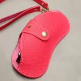 Estuche para lentes de diseño ergonómico y minimalista, confeccionado en cuero sintético con textura granulada. Cuenta con cierre magnético frontal, costuras a la vista en color contrastante y una correa de mano extraíble.