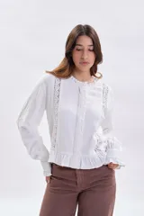 Blusa blanca de manga larga con detalles de encaje vertical en el frente, cuello con volados y terminación con volado en el ruedo. Presenta puños con volados y cierre frontal con botones.