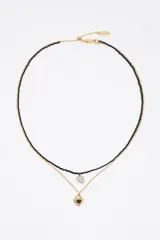 Collar doble dorado, compuesto por una tira corta de cuentas negras con un dije de perla y una cadena más larga con un dije de corazón esmaltado en negro.