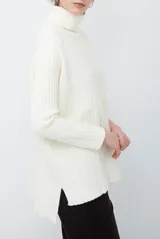 Polera de tejido acanalado en color blanco, con cuello alto, mangas largas y diseño de corte recto con aberturas laterales en el ruedo.