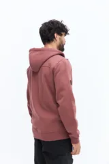 Campera de felpa color camel con cierre frontal, capucha ajustable con cordones negros y bolsillos laterales con cierre negro. Presenta un estampado pequeño en el pecho con texto en color oscuro.