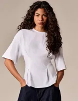 Top blanco de diseño estructurado, con mangas amplias y silueta entallada mediante pinzas frontales. Confeccionado en tela de algodón con caída firme y acabado minimalista.
