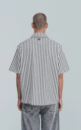Camisa de manga corta con cuello abierto y calce oversize, confeccionada en sarga liviana con estampado de rayas verticales en negro y blanco.