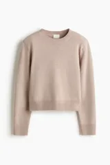 Buzo en punto fino suave de color beige con hombreras y ribete acanalado en cuello redondo, puños y bajo.