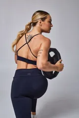 Top deportivo color beige con contorno inferior y tiras cruzadas en la espalda color borgoña. Cuenta con almohadillas removibles.