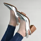 Zapatos stiletto destalonados de cuero color verde menta, con taco ancho de madera y hebilla metálica dorada de ajuste en el talón. Presentan punta fina y costuras visibles en el borde de la suela.