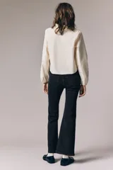 Jean de denim elástico color negro, de tiro alto, con cierre de botón y piernas acampanadas. Cuenta con bolsillos decorativos delanteros y bolsillos traseros.