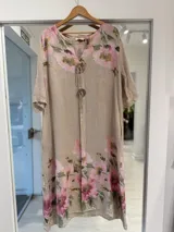 Vestido midi de lino color beige con estampado floral en tonos rosados y verdes, escote en V con cordones y botones decorativos de madera, de corte holgado y mangas cortas.