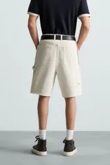 Bermuda relaxed fit confeccionada en tejido de algodón con efecto lavado. Presenta un diseño de cinco bolsillos, bolsillo multifunción en la pernera y tira lateral de estilo carpintero. Cuenta con cierre frontal con cremallera y botón.