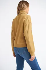 Buzo tipo polera de algodón, con cuello alto, mangas largas con puños y diseño holgado. Presenta una pequeña grifa metálica decorativa.