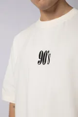 Remera oversize de algodón 100% premium, color blanco hueso, con bordado frontal "90's" en negro y un parche trasero con una imagen estilo videoclip de Nirvana.