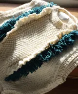 Chaleco tejido a mano en color crudo con panel central en punto arroz, vuelos laterales y flecos en contraste. Cuenta con cuello redondo a la base y sisas amplias.