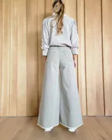 Pantalón de jean color beige, de corte recto y tiro alto, con ruedo deshilachado y cierre frontal con botón y cremallera.