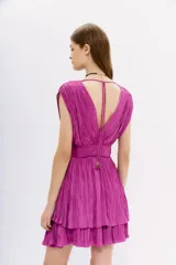 Vestido corto de color fucsia, confeccionado en tela con efecto crinkle. Presenta un diseño sin mangas con escote en V profundo tanto en el frente como en la espalda, cintura marcada y falda con volados. Incluye tiras de ajuste en los hombros con terminaciones metálicas.