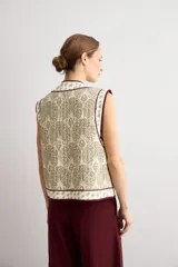 Chaleco capitoneado sin mangas, color crudo con estampado paisley y bordes ribeteados en tono bordó.