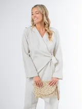 Conjunto de dos piezas confeccionado en lino color beige, compuesto por un pantalón de corte recto y un blazer cruzado con lazo ajustable en la cintura y escote en V.