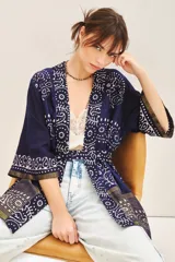 Saco tipo kimono de estilo artesanal, confeccionado en tela azul marino con estampado geométrico y floral en blanco y detalles metalizados. Presenta solapas anchas, mangas largas, lazo ajustable en la cintura y bolsillos laterales.