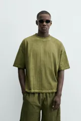 Camiseta de algodón de corte relajado (relaxed fit) con cuello redondo y manga corta. Presenta un tejido acanalado vertical (canalé) y un acabado ligeramente desgastado o lavado en tono verde oliva.