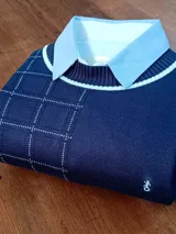 Sweater azul marino con cuello polo celeste, diseño de cuadros blancos y logo bordado en el frente.