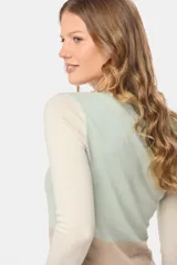 Buzo de tejido de punto con diseño de bloques de color en tonos verde menta, crema y beige. Presenta mangas largas y un panel inferior con textura de cableado.