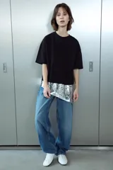 Camiseta negra de corte oversize, cuello redondo y manga corta. Presenta un bajo asimétrico con una aplicación de lentejuelas plateadas a contraste.