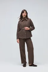 Camisa de lana fina sin teñir, color marrón, con diseño capitoneado y pespuntes decorativos. Presenta cuello clásico, cierre frontal con botones metálicos y dos bolsillos frontales tipo parche.