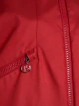 Chaqueta roja con capucha y cierre frontal con cremallera. Cuenta con bolsillos laterales con cremallera, un bolsillo con solapa en la manga izquierda y puños elásticos.