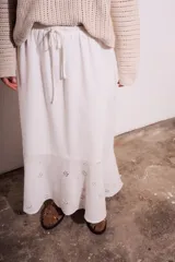 Falda larga blanca de viscosa y lino, con cintura elastizada y cordón ajustable. Presenta bordado calado con motivos florales en el ruedo.