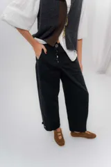 Pantalón de gabardina de algodón color negro, con calce barrel, cintura media baja, recortes de diseño y detalle de botones en el ruedo para ajustar el volumen.