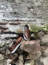 Zapatillas de cuero negro con diseño entretejido y suela blanca.