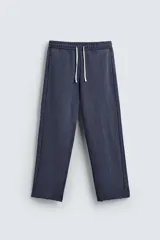 Pantalón jogger de corte wide fit confeccionado en algodón con interior de rizo. Presenta cintura elástica ajustable con cordón, bolsillos laterales y un bolsillo trasero de plastrón. Cuenta con un efecto lavado y acabados irregulares en el ruedo.