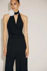 Body negro de cuello halter con escote drapeado pronunciado, detalle de flor blanca en relieve y espalda descubierta.