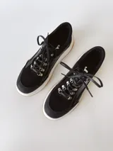 Zapatillas deportivas negras de cuero, con cordones y suela de goma blanca con base marrón.