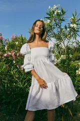 Vestido corto blanco de lino, con escote recto, mangas abullonadas 3/4 con elástico y falda con volantes.