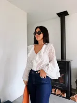 Blusa blanca con estampado de lunares, confeccionada en tela semitransparente. Presenta escote en V con volados frontales y mangas largas acampanadas con volados en los puños.